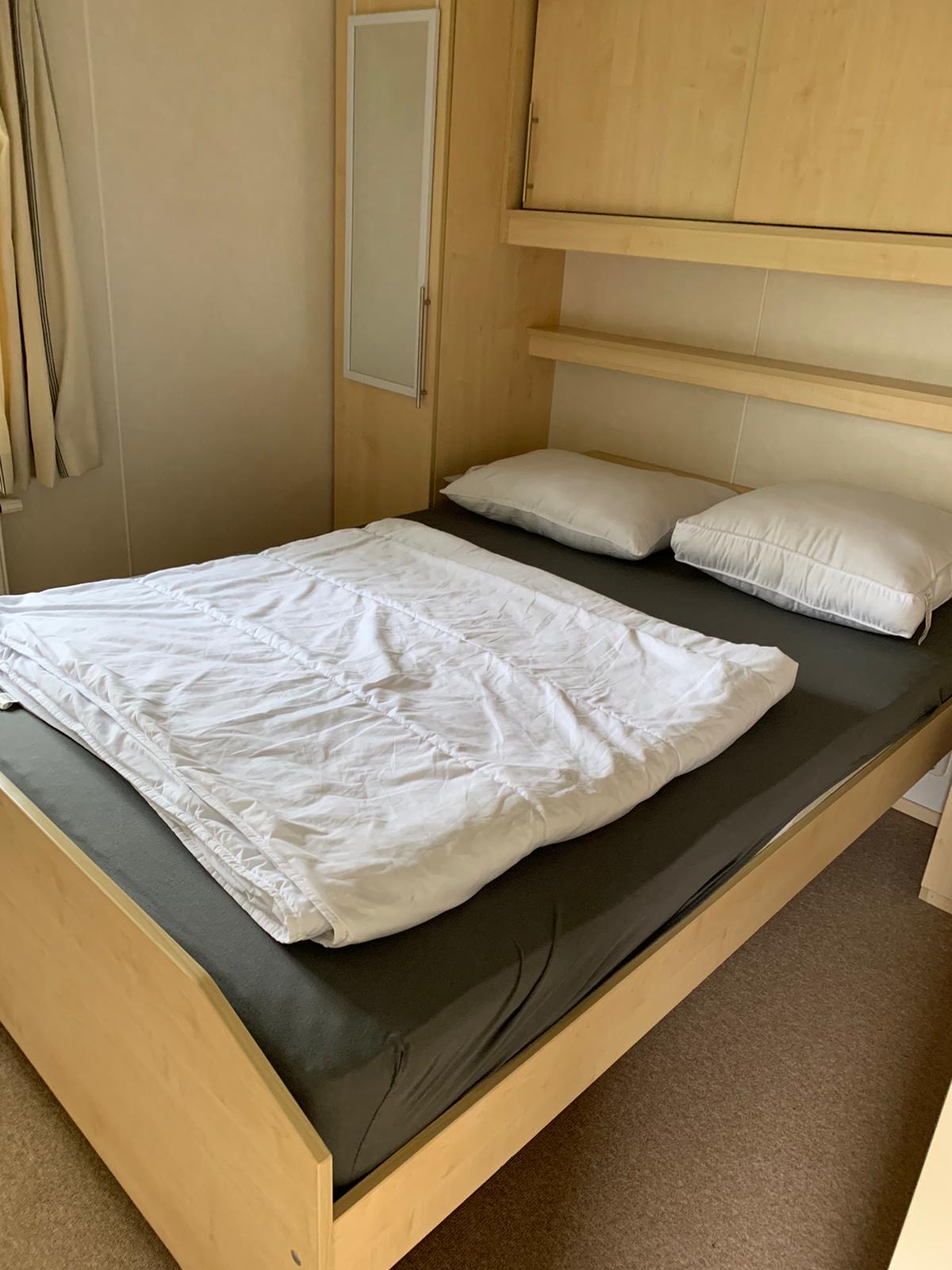 Houten tweepersoonsbed met houten kasten op de achtergrond.