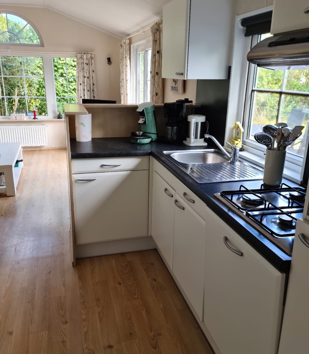 Open keuken met 4 pits gasfornuis, vaatwasser, magnetron en een ijskast met vriesvak.