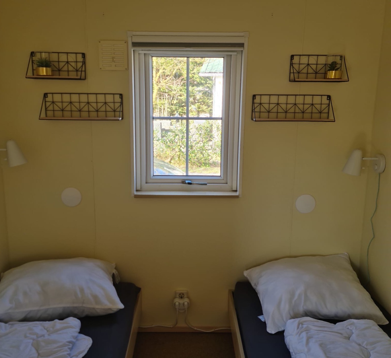 Kamer met twee eenpersoonsbedden met gele muren en een raam in het midden.