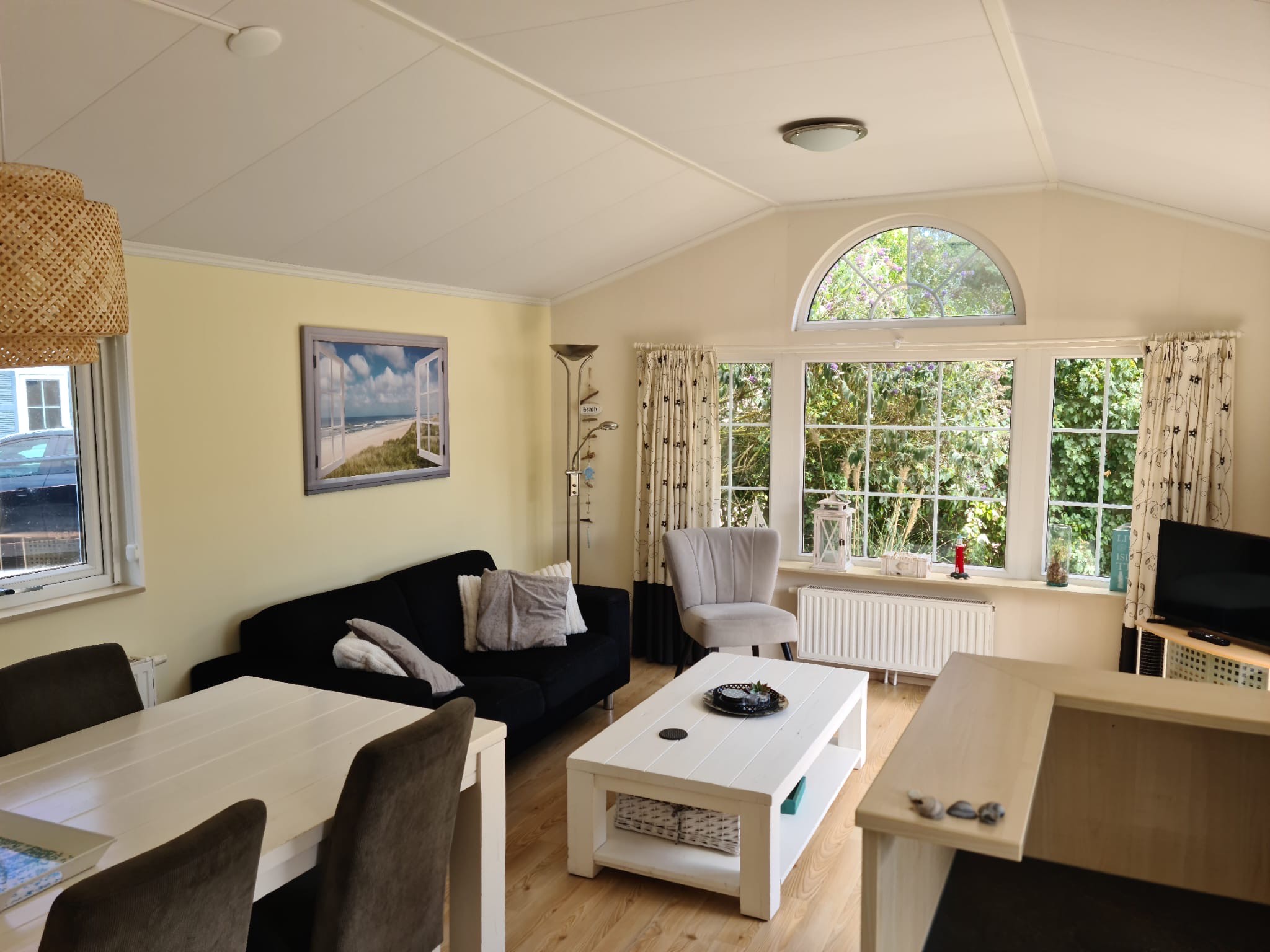 Woonkamer met aan de linkerkant een zwarte bank, in het midden een grijze tafel en aan de rechterkant een tv. 