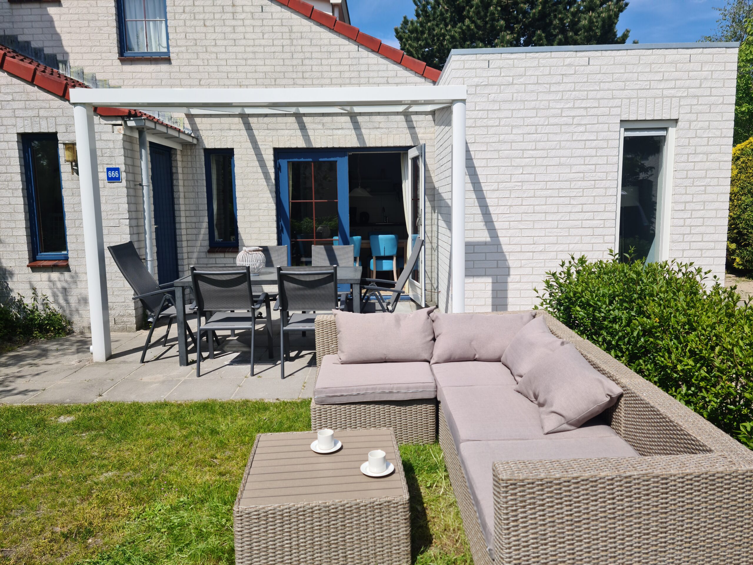 Tuin om het huis met overdekt terras en gazon met lounge set.