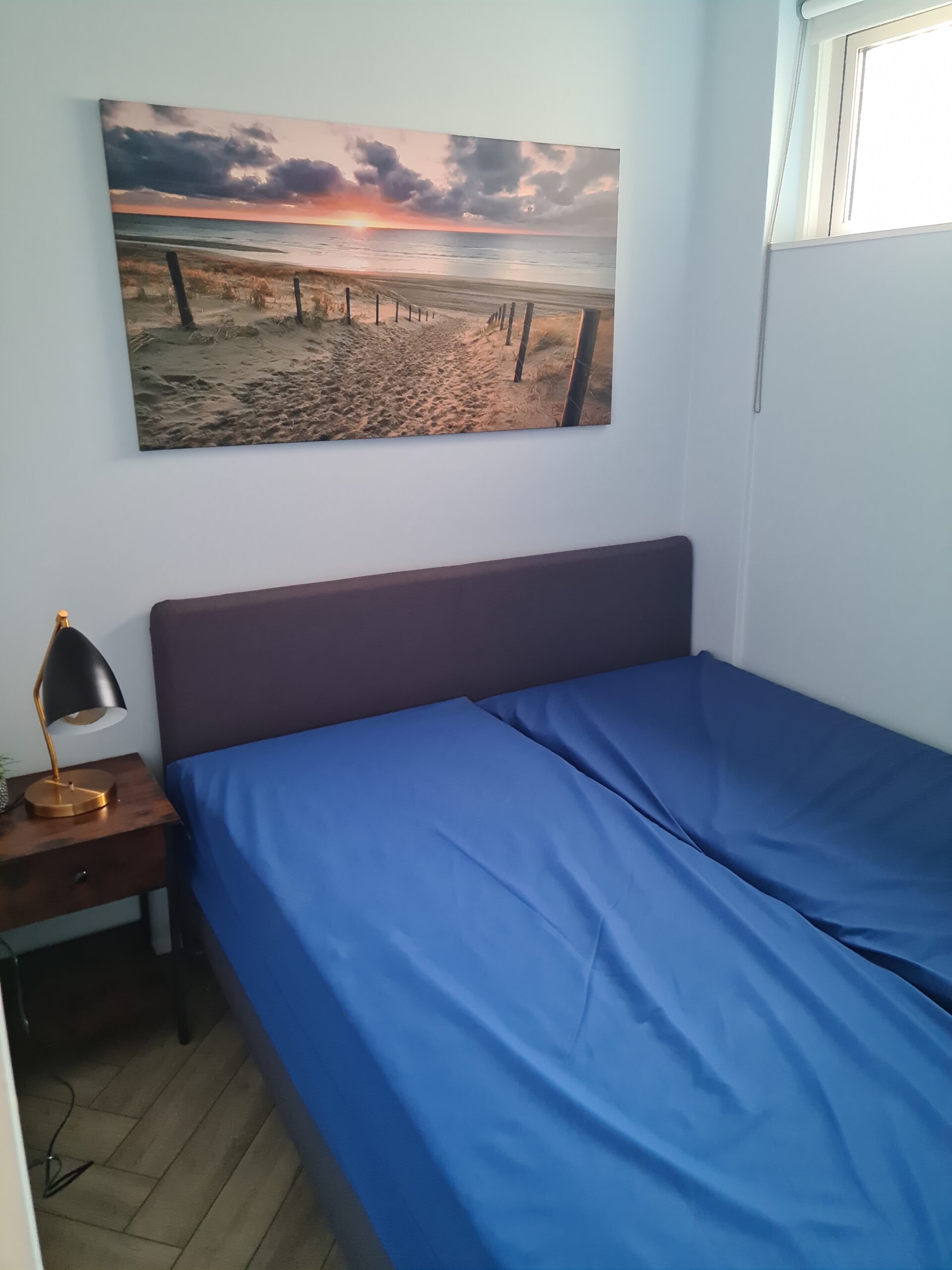 slaapkamer met 2 eenpersoons bedden die tegen elkaar staan, met schilderij op de achtergrond.