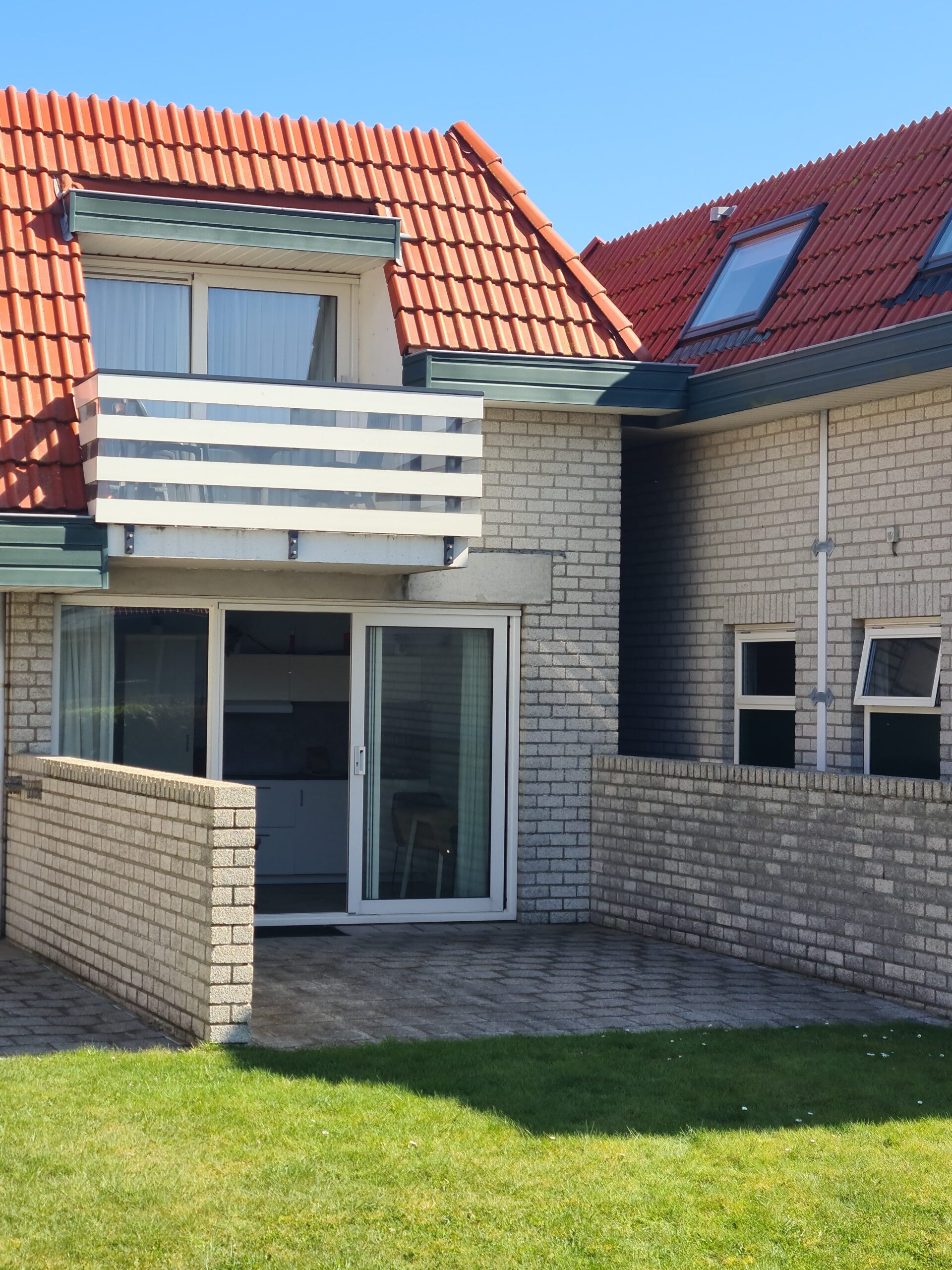 buitenkant appartement, foto genomen vanaf het centrale grasveld met uitzicht op het terras en schuifdeuren.