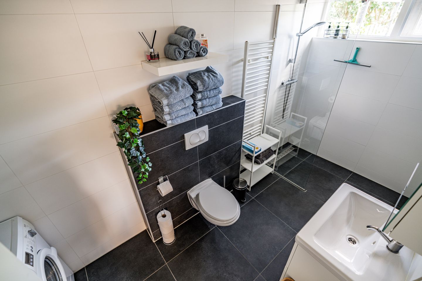 Moderne badkamer met inloopdouche, wastafel, toilet en een wasmachine.