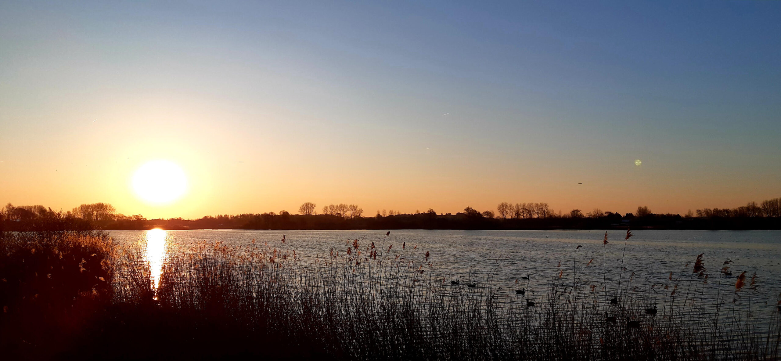 Foto van zonsondergang op het Oostduinse meer dat grenst aan het recreatiepark.